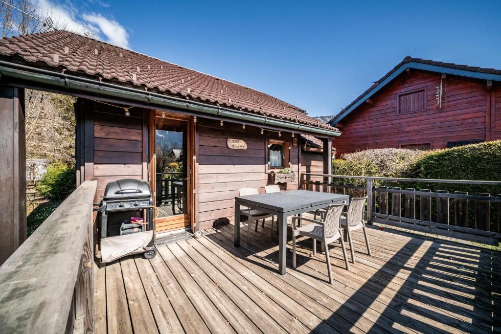 a wooden deck with a grill and a table and chairs at Chalet 6p - Le casse noisette in Verchaix