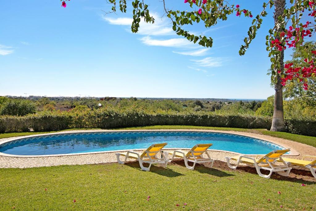 a swimming pool with four chairs and a tree at Casa do Barrocal in Almancil