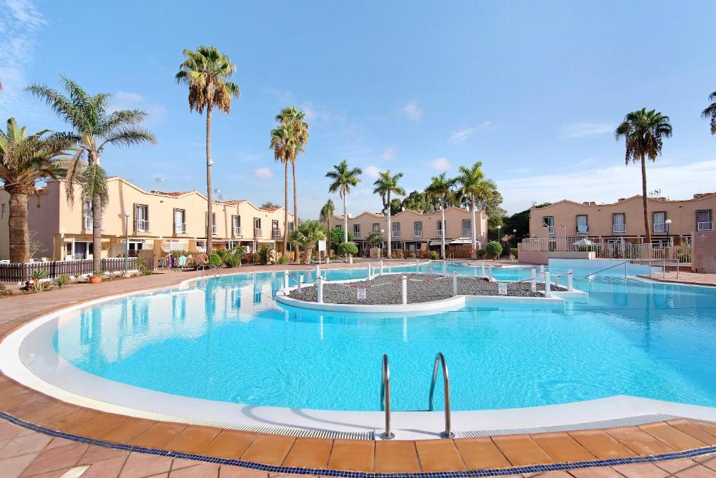 a large swimming pool with palm trees and buildings at Place Oasis Green Luxury Pool in Maspalomas