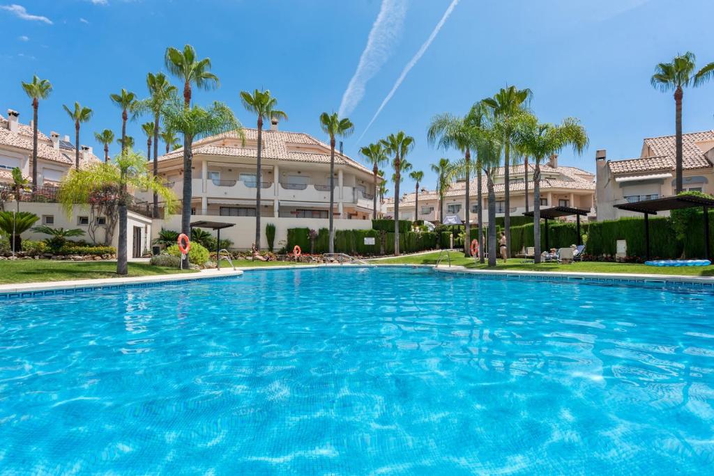 a large swimming pool with palm trees and buildings at Casa Sunshine in Marbella