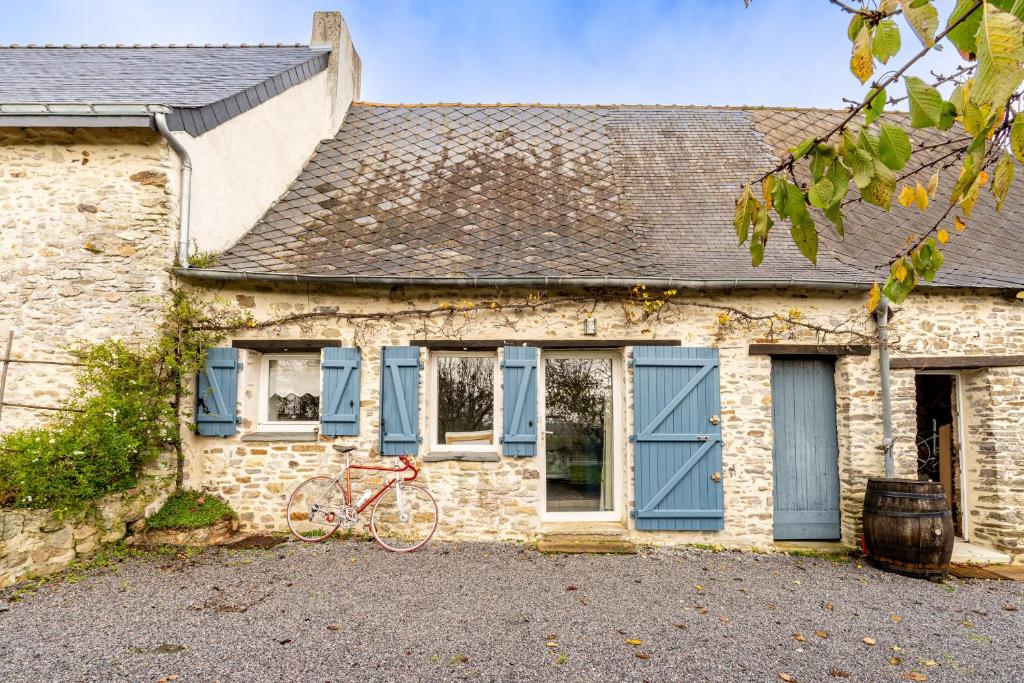 a red bike parked outside of a brick house with blue shutters at Charmante Longère La Meslière in Pannecé