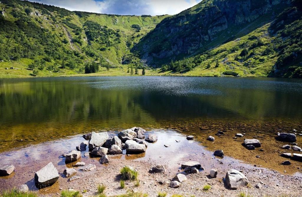 Calm mountain tarn with rocky shoreline reflecting green slopes inside a bowl-shaped valley.