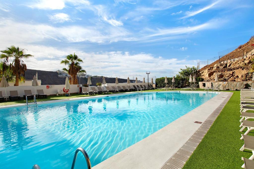 a large swimming pool with chairs and palm trees at Apartamento Joya in Puerto Rico de Gran Canaria