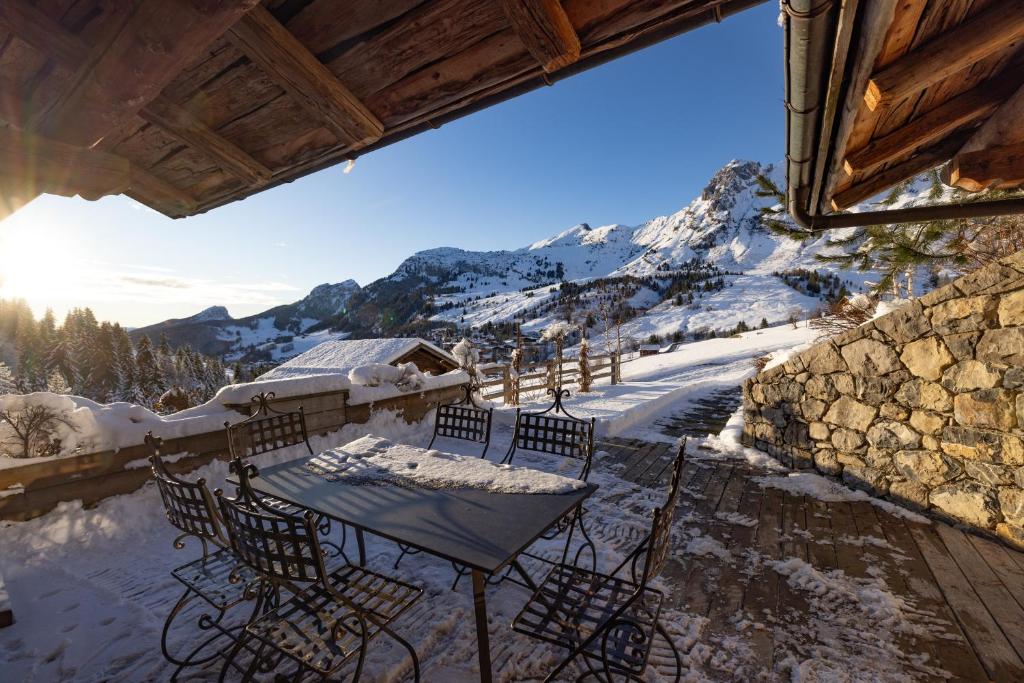 a table and chairs on a balcony with snow covered mountains at Coeur de neige 1724 in Le Grand-Bornand