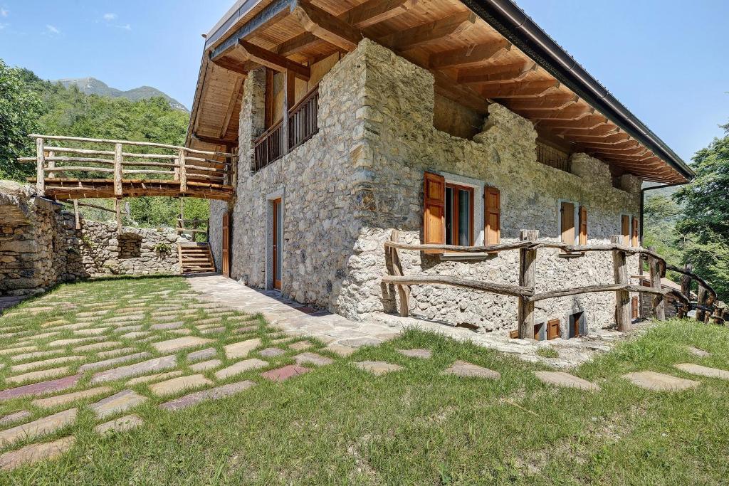 a stone house with a wooden roof and a grass yard at Casa al Mulino 1 in Tenno