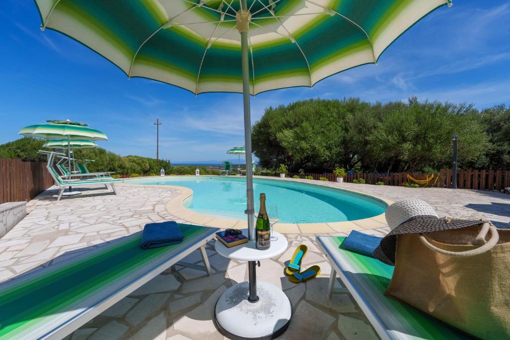 a pool with an umbrella and chairs and a bottle of wine at Casa Ginestre piscina e vista mare in Aglientu