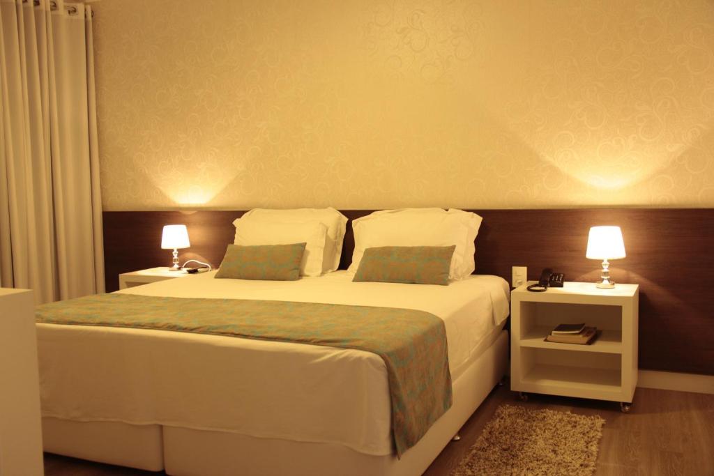 a bedroom with a bed and two night stands with lamps at Hz Hotel in Patos de Minas