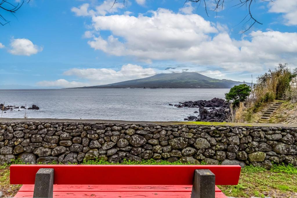 a red bench sitting next to a stone wall and a body of water at Casa da Praya in Horta