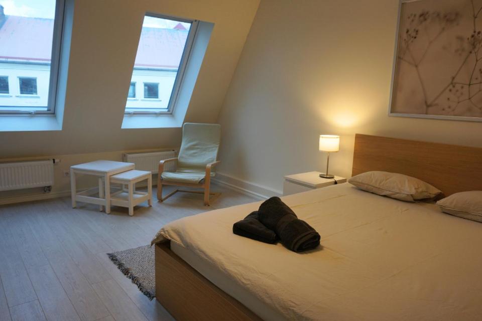 a bedroom with a bed and a chair and two windows at Kaiju Apartment 15 in Liepāja