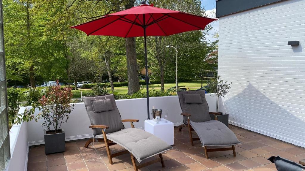a patio with three chairs and a red umbrella at Ferienwohnung Strandgut in Glücksburg