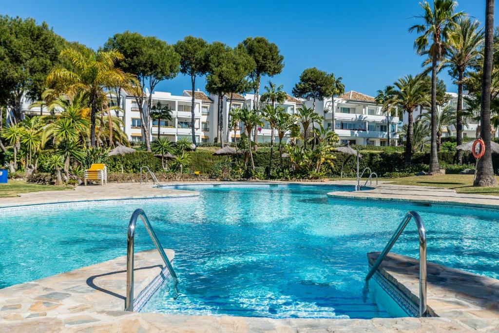 a swimming pool with palm trees and buildings in the background at 2bed apartment in Miraflores in Mijas