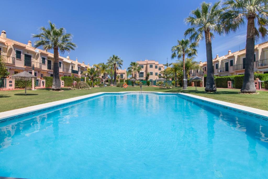 a large swimming pool with palm trees and buildings at Duplex Islantilla con piscina in Islantilla