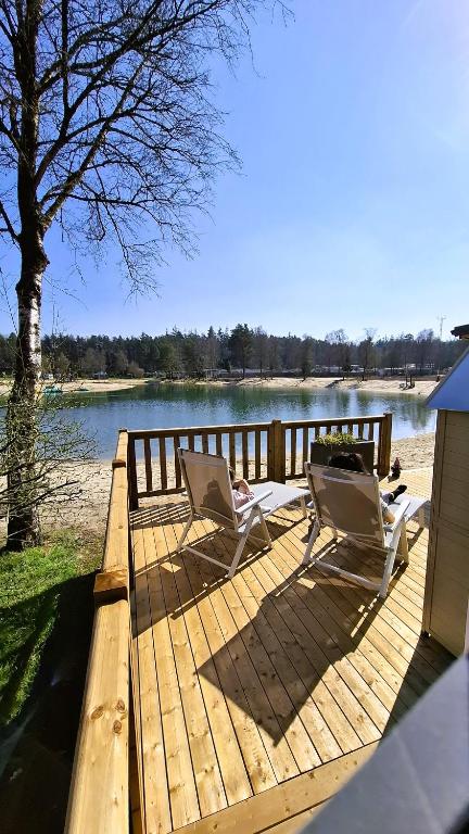 two chairs sitting on a wooden deck next to a lake at Sfeervol Veluws Meerhuisje luxe gezinschalet aan het water met opgemaakte bedden en handdoeken in Nunspeet