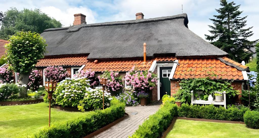 a house with a thatched roof and flowers at Lüttje Reethuus in Südbrookmerland