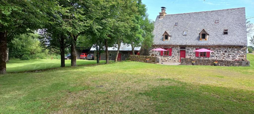 a stone house with pink umbrellas on a yard at Guidon Fourchette et table d'hôtes in Saint-Bonnet-de-Salers
