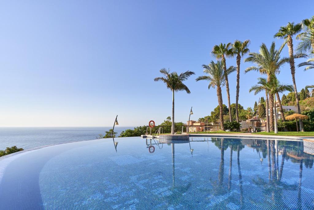 a swimming pool with palm trees and the ocean at Casa Palmeras in Almuñécar
