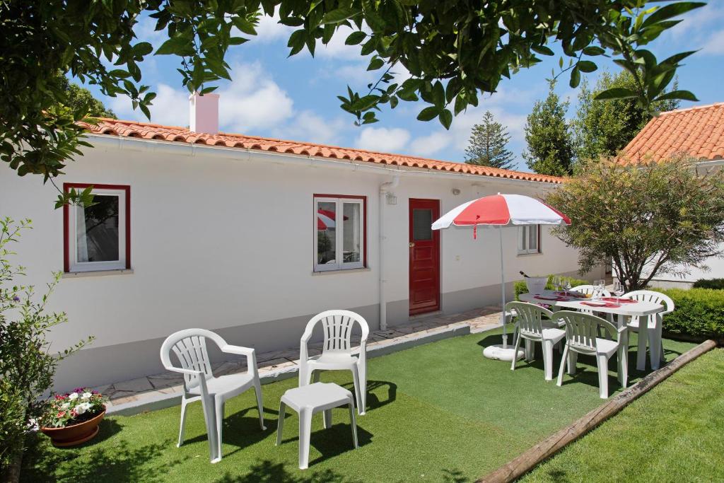 a patio with white chairs and a table and an umbrella at Páteo da Várzea 3 in Colares