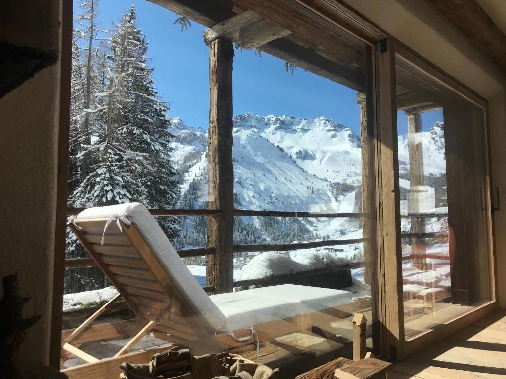 a chair in a window with a view of a mountain at Dolomites Luxe Cesa Del Louf in Arabba
