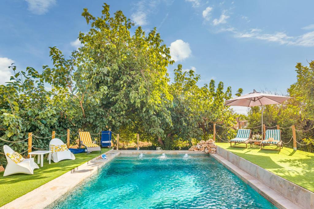 a swimming pool in a yard with chairs and an umbrella at Alegrías in Marratxí 