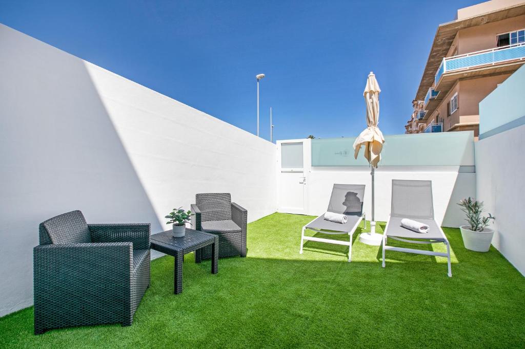 a patio with chairs and an umbrella and grass at Loft El Ramonal in Candelaria