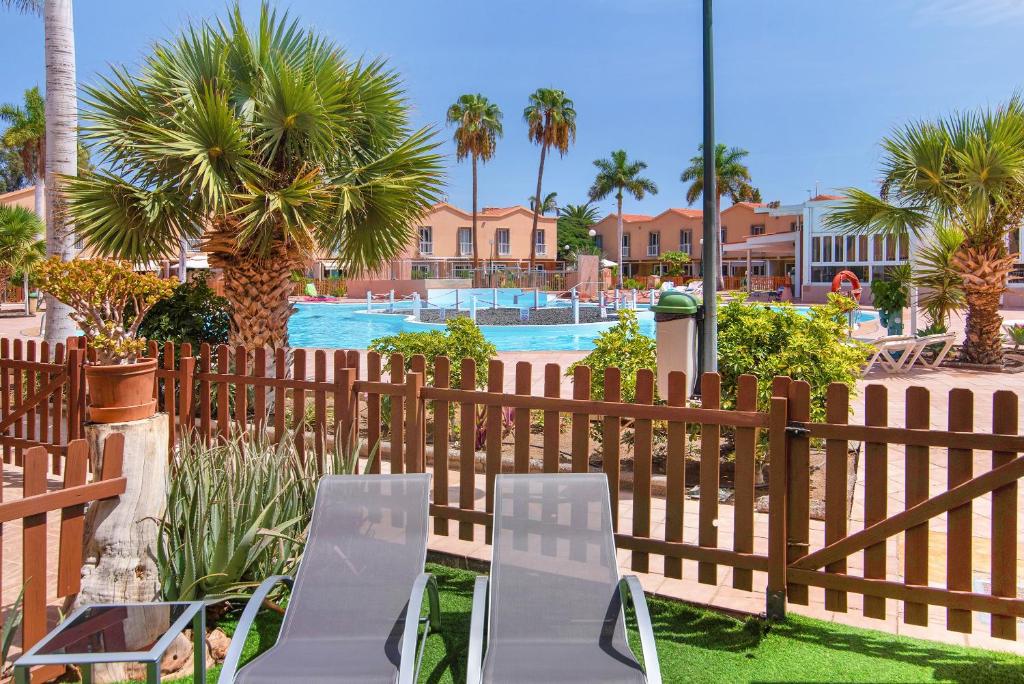 a fence with two chairs and a table in front of a pool at Oasis Pool View in Maspalomas
