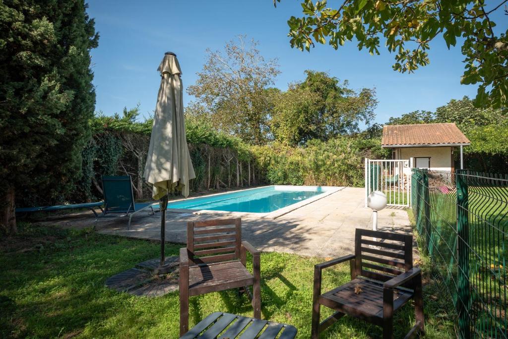 a patio with two chairs and an umbrella next to a swimming pool at Maison Blousson, Longère gersoise in Malabat