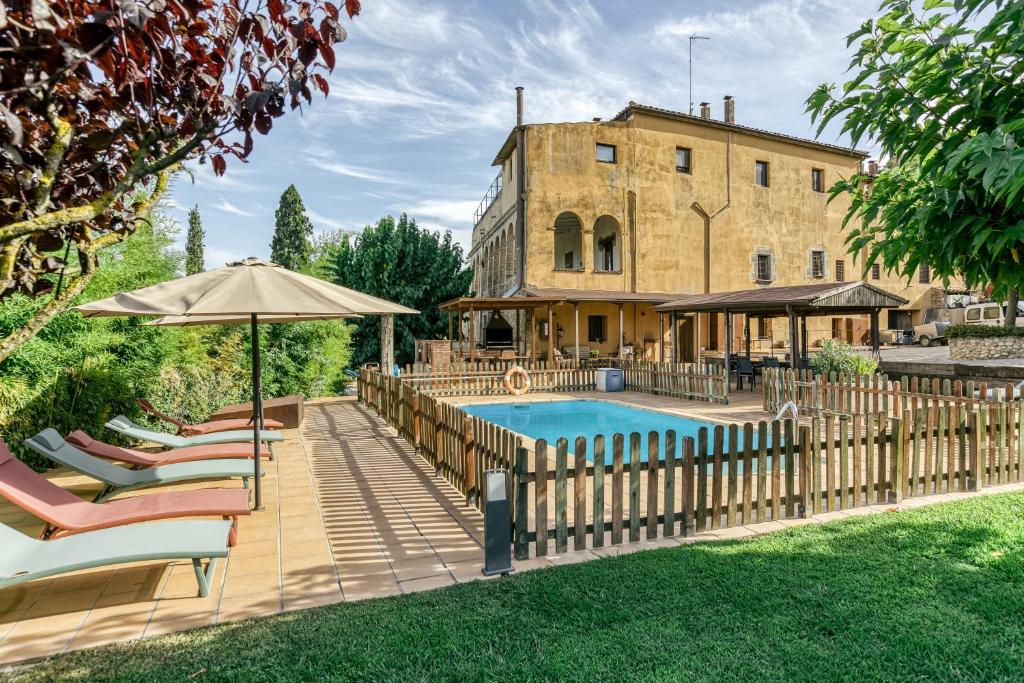 a pool with chairs and an umbrella next to a building at Mas Alba in San Esteban de Guialbes