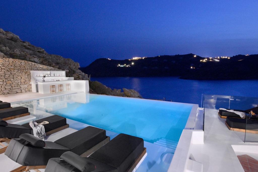 a swimming pool with chairs and the ocean at night at Wonderful Villa Chrysta in Mikonos