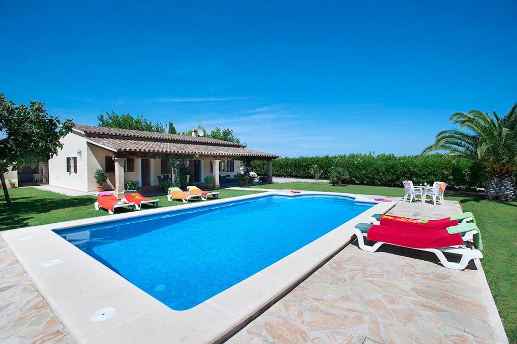 a swimming pool with chairs and a house at Villa Burgues in Alcudia