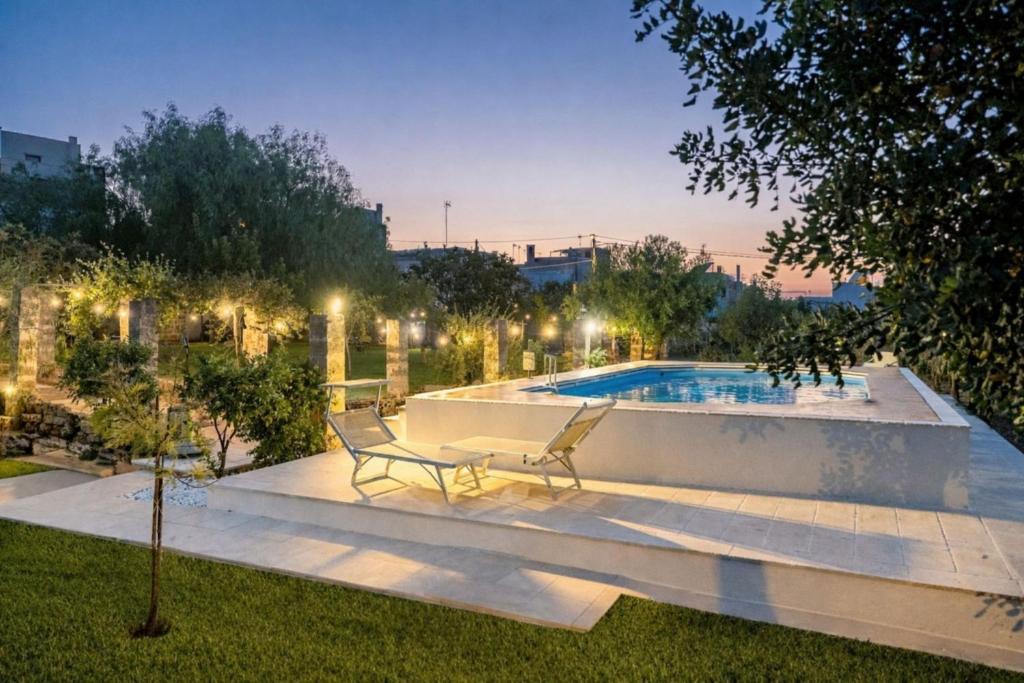 a swimming pool with two chairs in a yard at night at Masseria De Donno in Specchia
