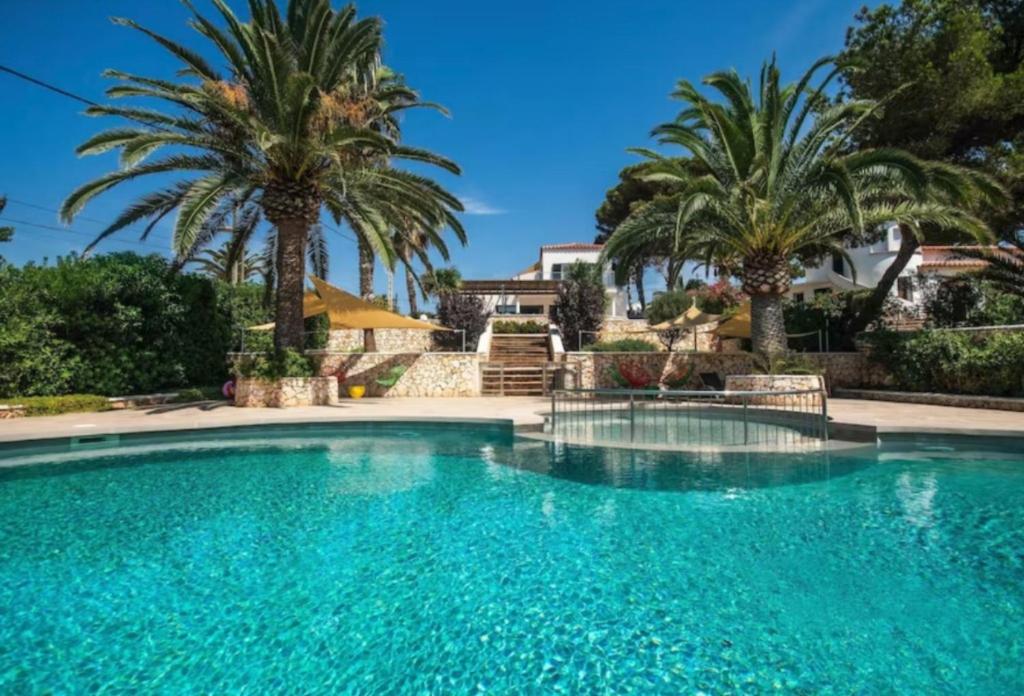 a swimming pool with palm trees and a house at Villa Linda in Punta Prima