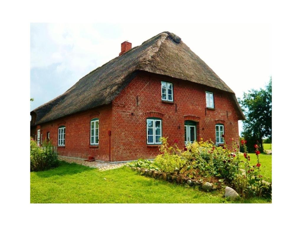 a large red brick house with a thatched roof at Ferienwohnungen Am Westerdeich in Rodenäs