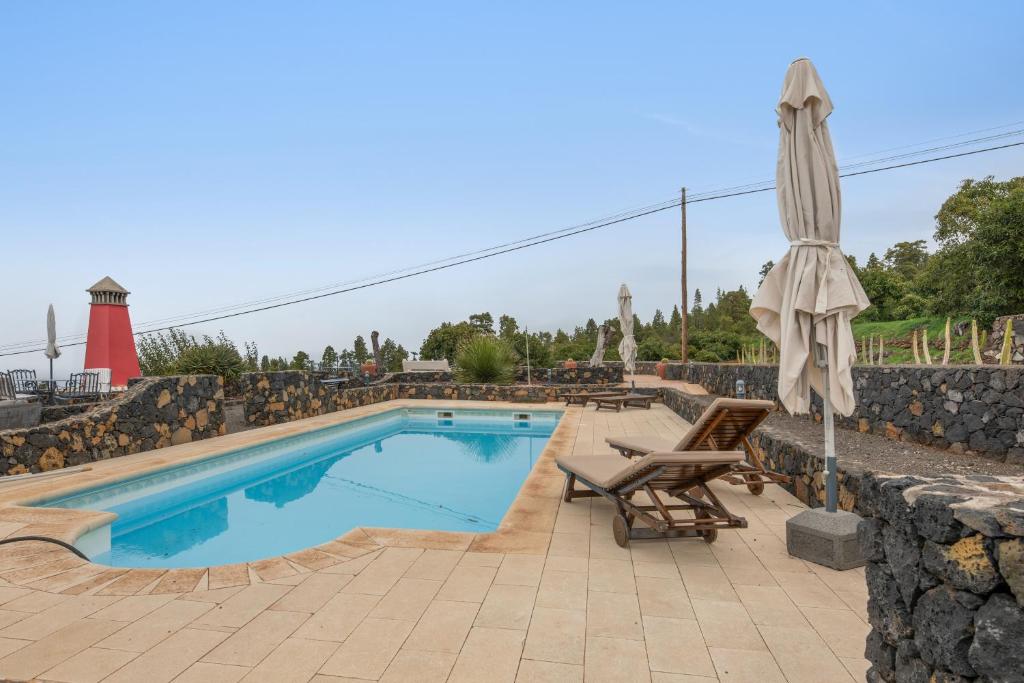 a swimming pool with a umbrella and a chair and a chaise at Apartamentos Los Aljibes in Las Tricias