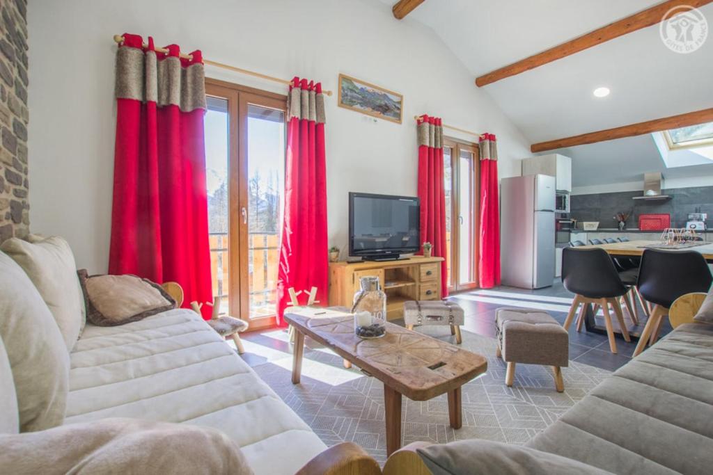 a living room with red curtains and a kitchen at Gîte Les Mélèzes in Termignon