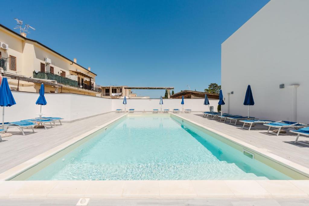 a swimming pool with chairs and blue umbrellas at Kairos San Vito Lo Capo in San Vito lo Capo