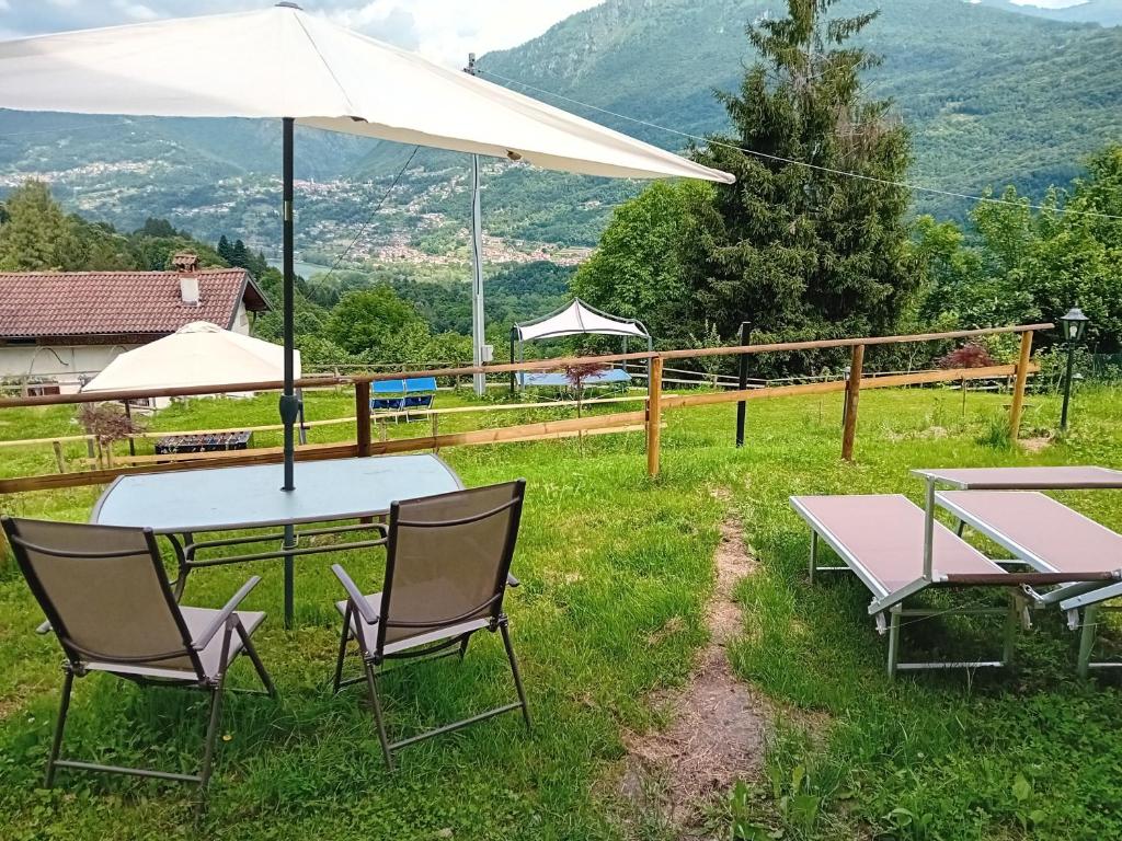 a table and chairs with an umbrella and mountains at Glamping C Selva Tenda Ciliegio in Piano Porlezza