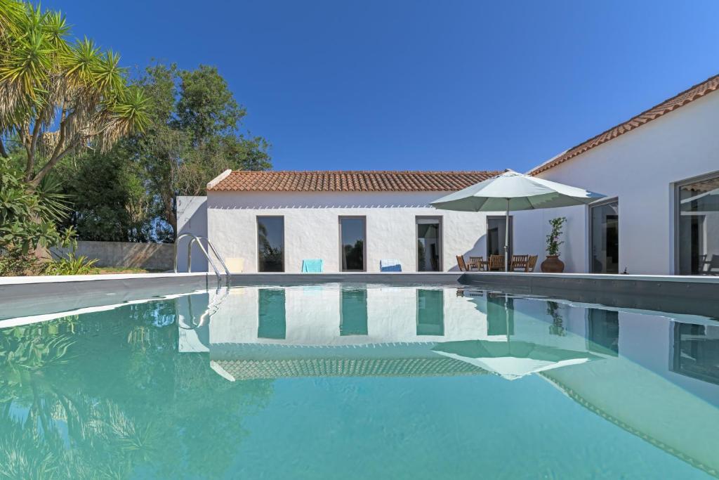 a swimming pool with an umbrella next to a house at Espaço Fataca - Sw Alentejano in São Teotónio