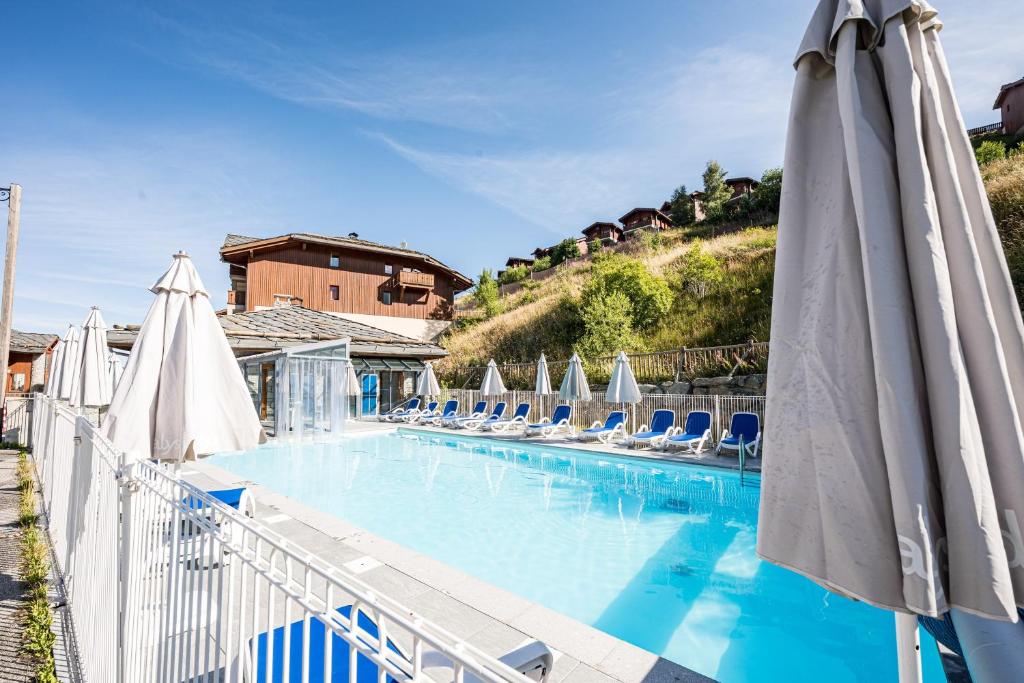 a large swimming pool with chairs and umbrellas at Appartement Ski Valmeinier in Valmeinier