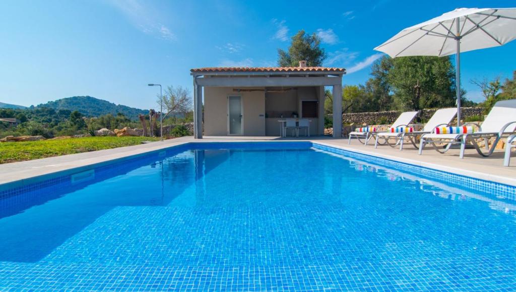 a swimming pool with chairs and an umbrella at Can Colomer Ferragut in Artá
