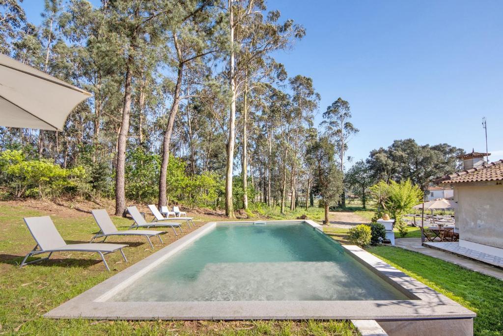 a swimming pool in a yard with chairs and an umbrella at Villa da Floresta in Arcos