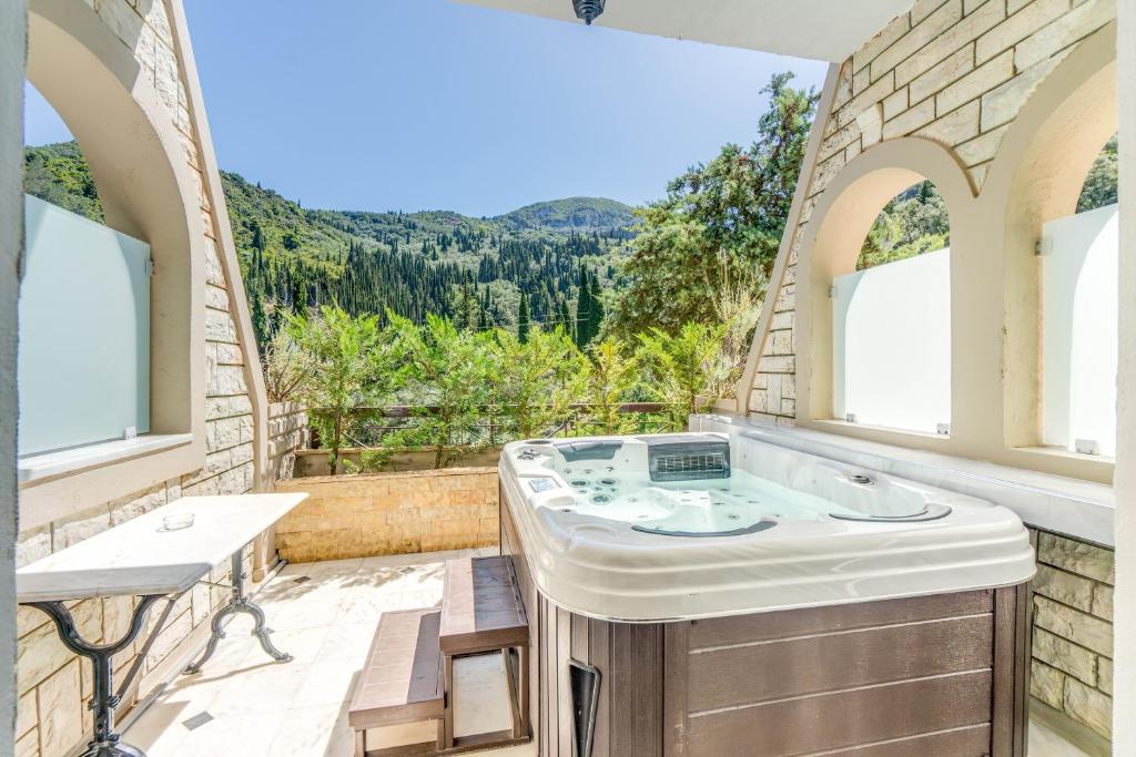 a bathroom with a tub and a balcony with mountains at Doliva Studio John private jacuzzi in Agios Gordios