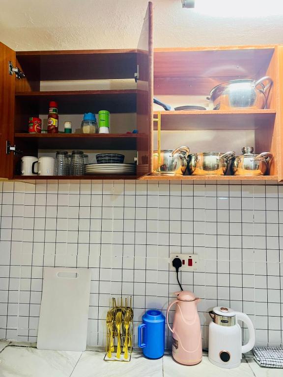 a kitchen with white tiled walls and shelves with utensils at Nimaai Apartment in Narok