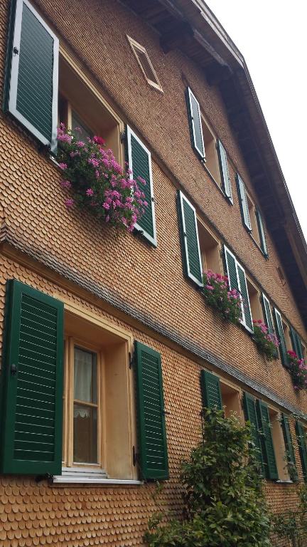 a brick building with green shuttered windows and flowers at Appartement Moosmann in Mellau