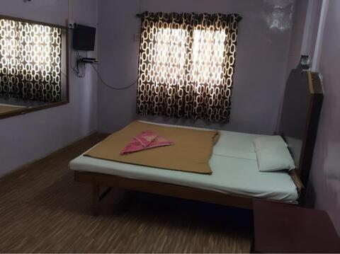 a small bed in a room with two windows at Laxmi Lodge in Pune
