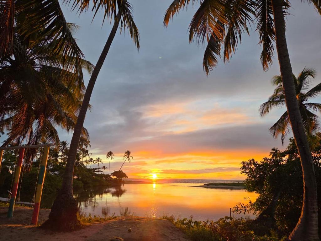 a sunset over a body of water with palm trees at Pousada Plenamar in Maragogi