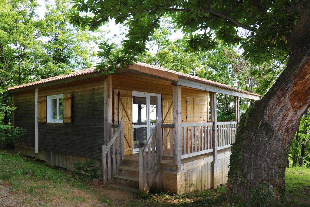 a wooden cabin with a porch and a tree at Maisons Cozy - Mas Lachamp in Gravières