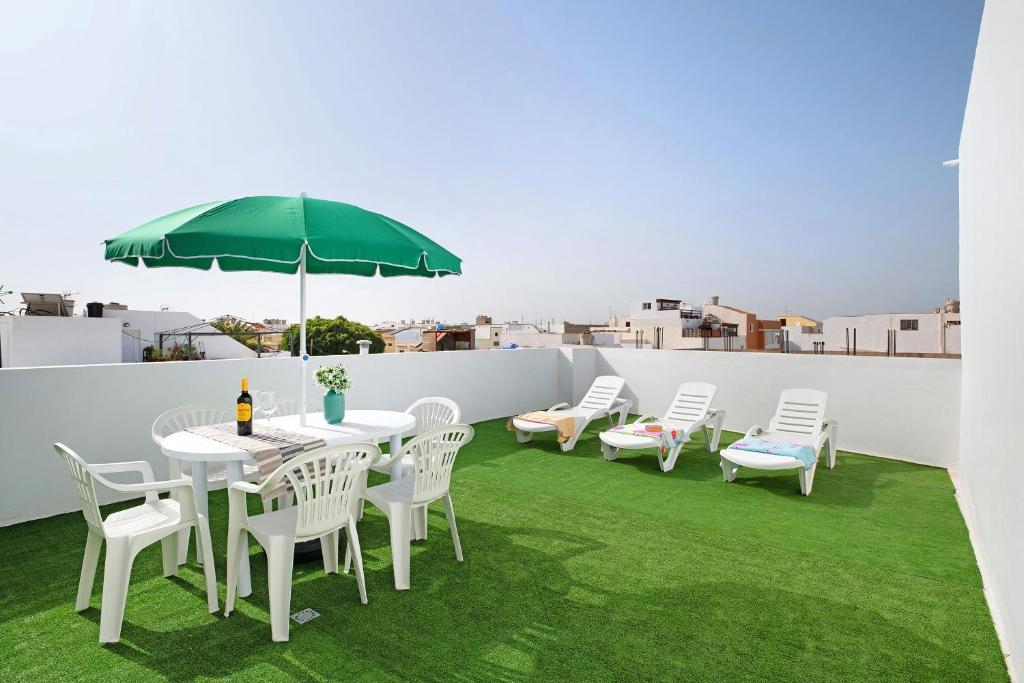 a patio with white chairs and a table with a green umbrella at Campo Amor Bajo in Arrecife