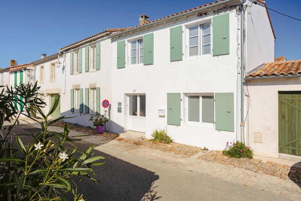 a white building with green shutters on a street at Chambres d’hôtes Chantal Hereaudeau in Ars-en-Ré