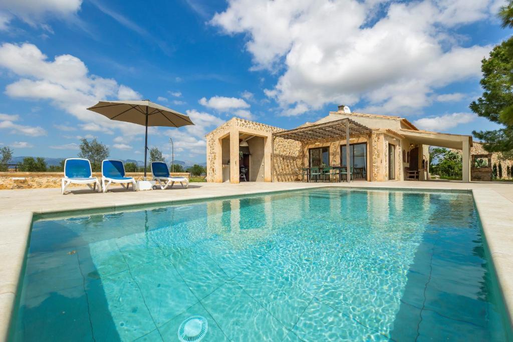 a pool with chairs and an umbrella in front of a house at Sa Caseta Biniali in Biniali