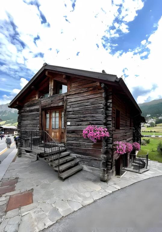 a small log cabin with pink flowers in front of it at La Coccinella Livigno in Livigno
